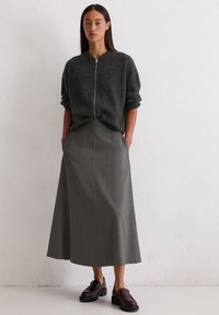 Grå oversized zip-up genser kombinert med et langt, strukturert grått skjørt og mørk burgunder slip-on sko. Glatte teksturer, minimal design.