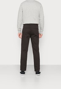 Zwarte katoenen broek met een rechte snit en achterzakken, gecombineerd met een lichtgrijs sweatshirt en zwarte sneakers.