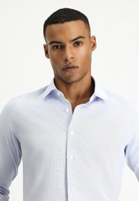 Lichtblauw overhemd met knoopsluiting en een subtiel textuurpatroon, voorzien van een klassieke kraag en lange mouwen met knoopmanchetten.