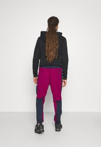 Svart huvtröja i kombination med färgblockerade träningsbyxor: djup lila och marinblå med sidodetaljer, som har en tight passform och elastiska ärmslut.