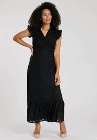Schwarzes Wickelkleid mit kurzen Rüschensäumen, strukturiertem Wellenmuster und gestuftem Saum. Hergestellt aus leichtem Stoff.