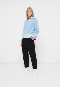 Lichtblauwe geribde trui met een ronde halslijn, gelaagd over een geruite blouse, gecombineerd met zwarte cropped broeken en witte sneakers.