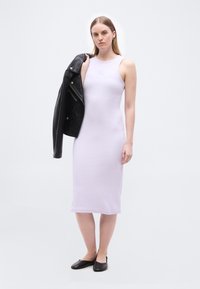 Γυναίκα που φοράει μωβ μίντι φόρεμα χωρίς μανίκια και μαύρες μπαλαρίνες, κρατώντας ένα μαύρο δερμάτινο μπουφάν στον ώμο της, με φόντο λευκό.