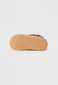 Sko såle med teksturert gummi, i beige farge, med spor for grep, og avrundet tåområde med tre avrundede gripe mønstre.
