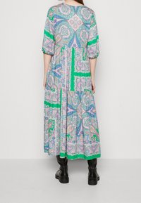 Dlouhá šaty s barevným paisley vzorem v růžové, zelené a modré barvě. Tříčtvrteční rukávy a vícevrstvová sukně. Nošeno s černými botami.