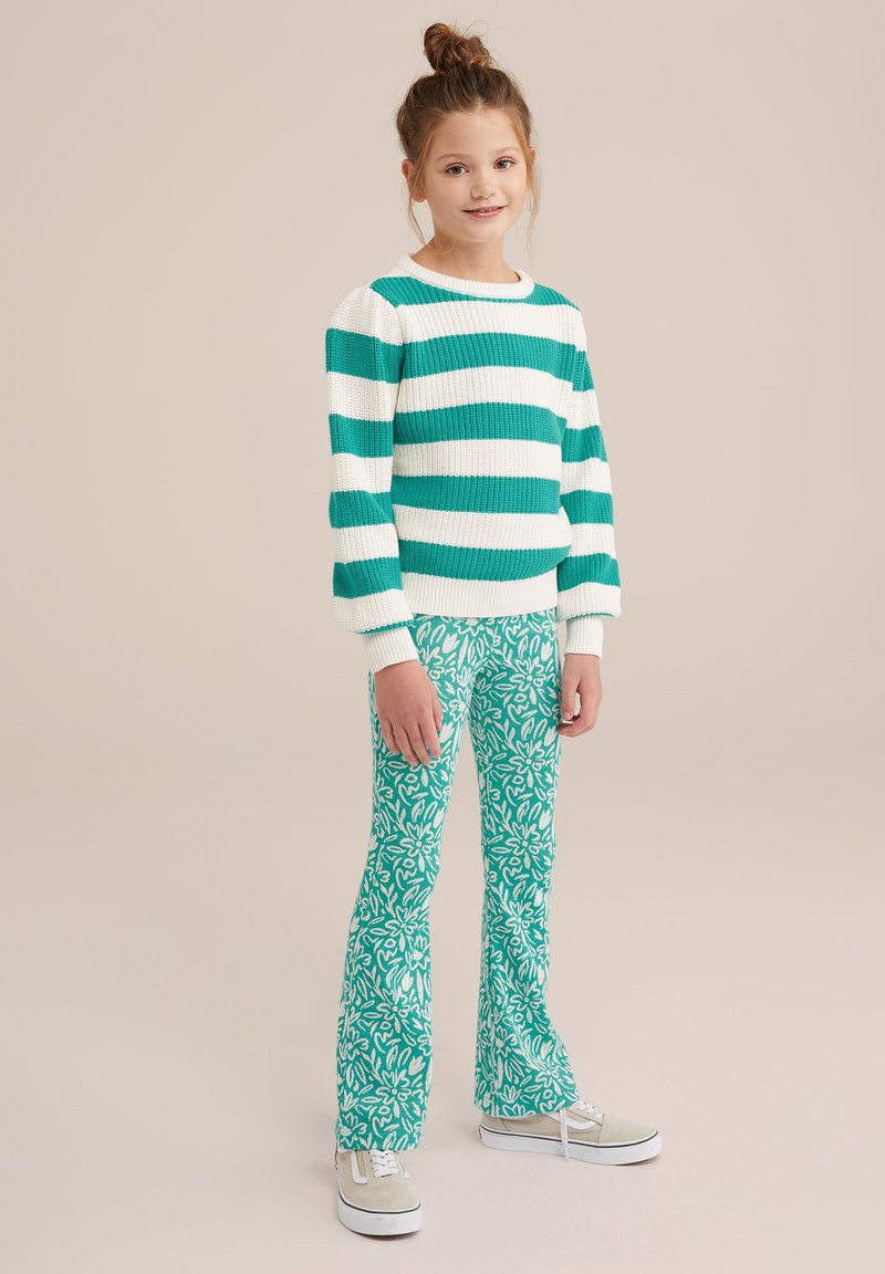 Pulover tricotat cu dungi verzi și albe, cu mâneci lungi, asortat cu pantaloni evazați verzi cu un model floral. Tenisi cu accente albe și crem.