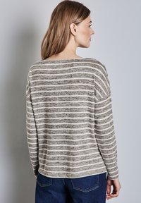 Grijs en crèmekleurig gestreept long-sleeve shirt met een brede halslijn en een ontspannen pasvorm, gecombineerd met donkerblauwe denim broek. Getextureerde stof.