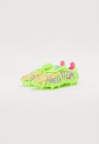 Des chaussures de football jaune-vert vif avec un motif texturé, des accents roses et un logo "PREDATOR" audacieux. Conçues pour l'adhérence avec des crampons moulés.