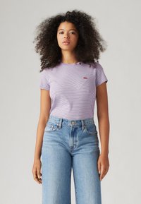 Purple striped short-sleeve t-shirt with a round neckline and a small red logo patch, paired with high-waisted light blue wide-leg jeans.