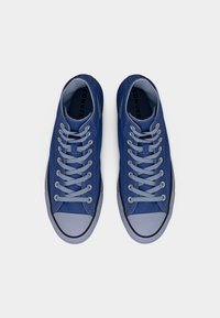 Ζευγάρι μπλε χαμηλά sneakers Converse με ανοιχτό μπλε κορδόνια και λαστιχένιες μύτες, σε προβολή από πάνω σε λευκό φόντο.