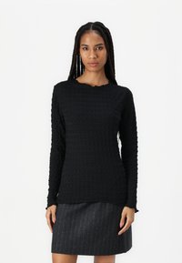 Svart teksturert langermet topp med bølget hals, kombinert med en mørkegrå rutete skjørt. Begge plaggene har en tettsittende design.
