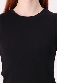 Svart ribbad ärmlös topp med rund halsringning. Texturen är slät med en figurnära design som betonar en strömlinjeformad silhuett.