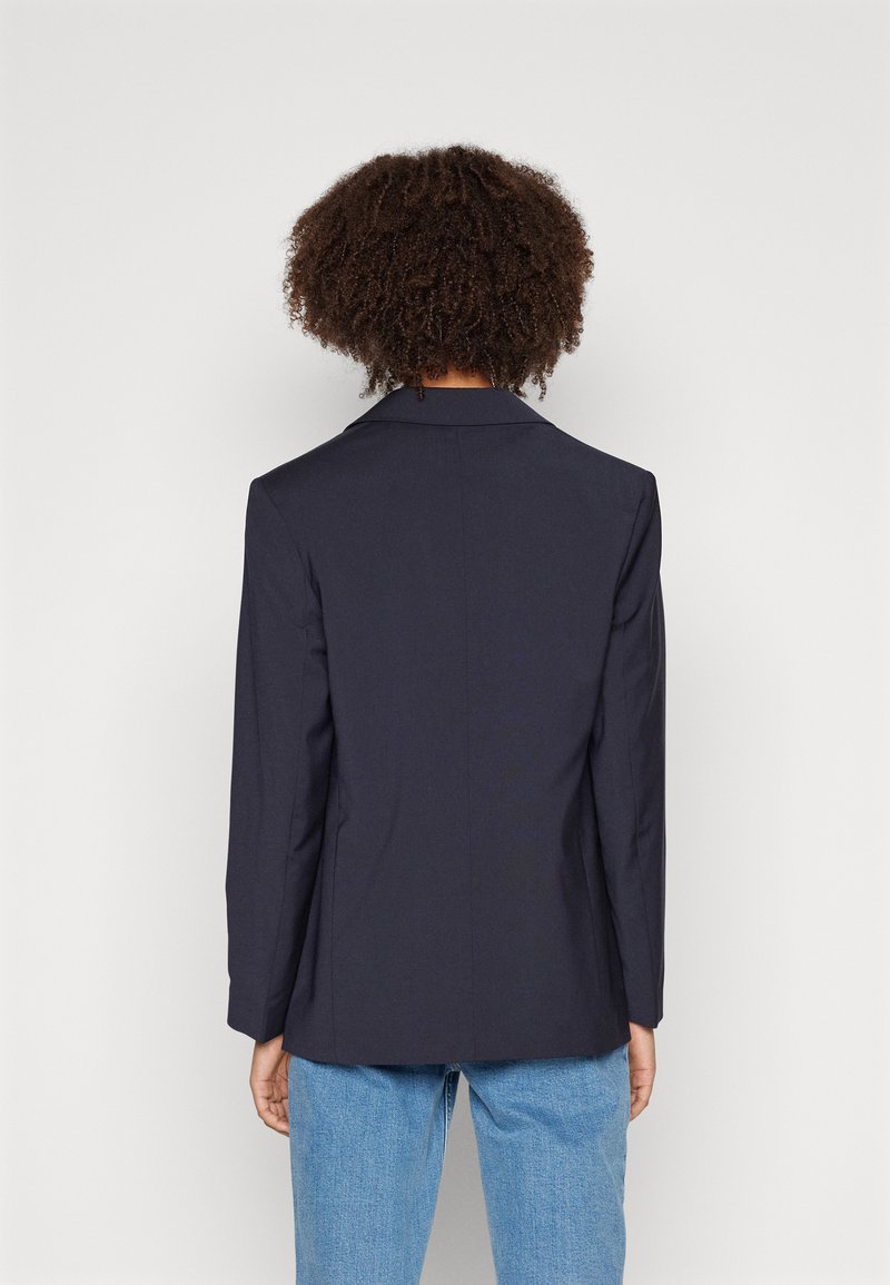Blazer marine avec revers cranté, fente simple et manches longues, associé à un jean bleu clair. Fabriqué en tissu lisse avec une coupe ajustée.