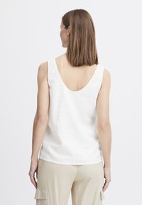 Weißes Leinen-Top ohne Ärmel mit tiefem Rückenausschnitt. Hat eine entspannte Passform und ein einfaches Design, kombiniert mit hellen, lässigen Hosen.