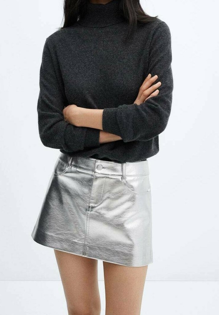 Pull à col roulé gris et mini-jupe argentée métallique. Le pull a des manches longues ; la jupe est ornée de boutons et présente une texture lisse et réfléchissante.
