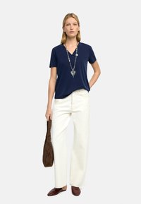 Granatowy T-shirt z dekoltem w serek, luźny fason, zestawiony z białymi szerokimi spodniami dżinsowymi. Uzupełniony długim srebrnym naszyjnikiem i brązową plecioną torbą, ciemnymi balerinkami.