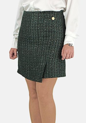 Falda texturizada verde con diseño envolvente, adornada con un botón dorado en la cintura y un dobladillo a la altura de la rodilla.