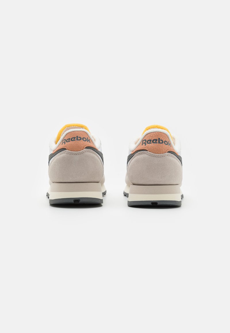 Baskets Reebok avec un dessus blanc et gris, des accents en suède beige et une doublure jaune. Texture lisse avec une semelle rembourrée.