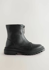 Bottine noire avec semelle épaisse à crampons et fermeture éclair à l'avant, finition mate lisse et bout rond sur un fond neutre clair.