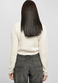 Weißer, fluffiger Pullover mit langen Ärmeln, kombiniert mit dunklen, verblichenen Jeans, die zwei Gesäßtaschen haben. Das Outfit hat eine lässige Passform.