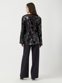 Veste noire en sequins floraux avec une texture lisse, dotée de manches longues et d'une coupe ajustée, associée à un pantalon noir à jambes larges.