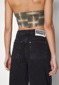 Grön- och rosa rutigt kort topp med rak skärning, parat med högmidjade svarta jeans med synlig etikett och bakfickor.