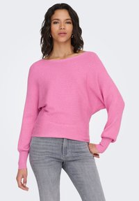 Maglione rosa a coste con ampio scollo a barca e maniche lunghe. Abbinato a jeans grigio chiaro, con vestibilità comoda.