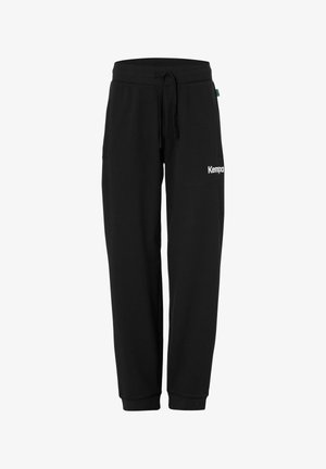Pantalon de survêtement noir à cordon de serrage avec des poignets élastiques et un logo blanc "Kempa" sur la partie supérieure de la cuisse droite.
