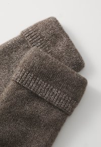 Calze marroni lavorate a maglia con una consistenza morbida, dotate di un bordo a costine e fili metallici intrecciati per un ulteriore dettaglio visivo.