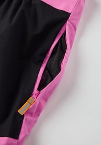 Vaaleanpunaiset ja mustat urheilushortsit, joissa on vetoketjullinen tasku verkkomateriaalilla, oranssi vetoketjun veto ja kontrastivärinen paneelimuotoilu.
