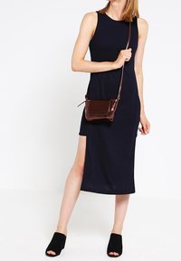 Marinblå ärmlös klänning med sidoklyfta, i kombination med en liten brun crossbody-väska och svarta öppen-toe-mules. Slätt tyg, enkel design.