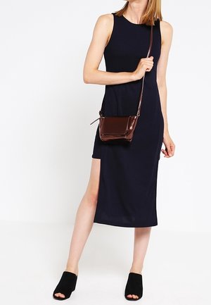 Vestido sin mangas azul marino con abertura lateral, combinado con un pequeño bolso cruzado marrón y mules negros destalonados. Tejido suave, diseño sencillo.