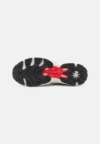 Shoe sole featuring a black rubber base, red midsole accents, textured gripping patterns, and a distinct logo detail in the center.