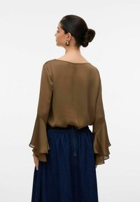 Brun, genomskinlig blus med vida ärmar, parat med en mörk denimkjol. Blusen har en vid halsringning och en flödande silhuett.