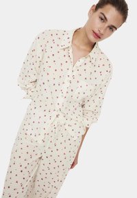 Set di pigiama in cotone avorio con motivo floreale, composto da una camicia con bottoni e pantaloni con cordoncino. Presenta piccoli fiori multicolori su sfondo a quadretti.