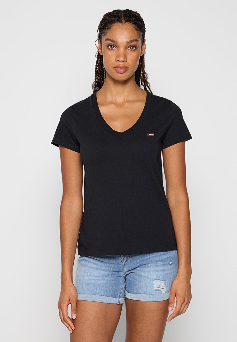 Schwarzes Baumwoll-T-Shirt mit V-Ausschnitt und kurzen Ärmeln, mit einem kleinen roten Logo auf der linken Brust. Getragen mit Jeans-Shorts.