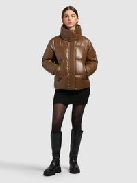 Brun puffjacka med hög krage, blank finish och quiltad mönster. Svarta knähöga stövlar, kombinerade med en ribbad svart kjol.