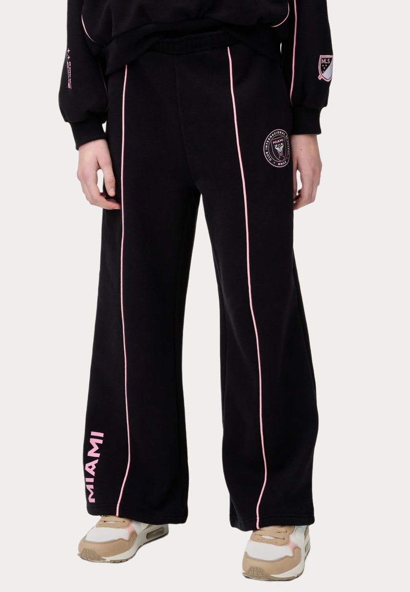 Pantalones de chándal negros con franjas laterales rosas, cinturilla elástica y un logo de Miami. Fabricados en tela suave. Presentan un diseño de pierna ancha.