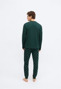 Top verde de manga larga con cuello redondo y pantalones de pijama verdes a juego con un patrón de nubes blancas, ambos de material suave.