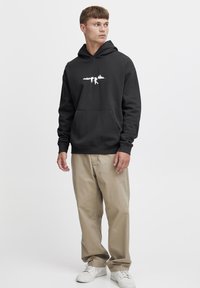 Sudadera negra con un diseño gráfico blanco en el pecho, combinada con pantalones beiges y zapatillas blancas. Tejido suave y bolsillo tipo canguro.
