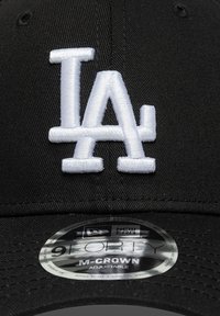 Cappello da baseball nero con logo "LA" ricamato in bianco, dotato di visiera curva e cinturino regolabile, etichettato "New Era 9FORTY M-CROWN".