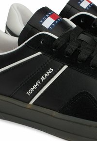 Czarne skórzane trampki z zamszowymi akcentami, białymi paskami i metką z logo w kolorach niebieskim, czerwonym i białym. Czarne sznurowadła i gumowa podeszwa.