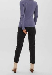 Haut violet texturé à manches longues associé à un jean noir fuselé. Les chaussures sont beiges avec un talon épais. La vue de dos montre une coupe décontractée avec des poignets côtelés.