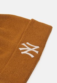 Knit beanie in burnt orange with a folded cuff. Features a white embroidered logo on the side, textured fabric, and casual design.