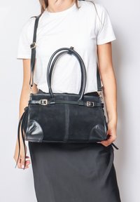 Borsa nera realizzata in suede e pelle con manici doppi, una tracolla removibile e accenti laterali. Presenta un design strutturato.