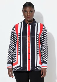 Camisa de manga larga con botones que presenta un patrón geométrico en negro, blanco, rojo y azul, con rayas en contraste y una textura de tela suave.