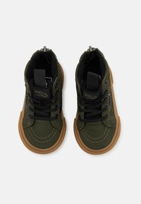 Gröna kanvas högstols-skor med svarta detaljer, svarta snören, en brun gummisula och sömnadsdetaljer på tåområdet.