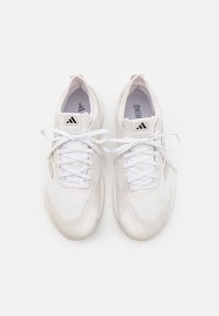 Zapatillas deportivas blancas hechas de tejido texturizado, con un diseño de cordones, una plantilla acolchada y un logo negro en la lengüeta.