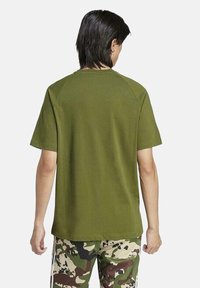 Camiseta de algodón verde oliva con mangas cortas y cuello redondo, que presenta un diseño sencillo sin logotipos ni adornos.