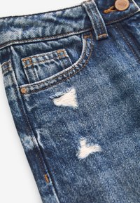 Jeans in denim blu con aree rovinate, caratterizzati da cuciture marroni e dettagli in rame, inclusi un bottone e dettagli delle tasche.